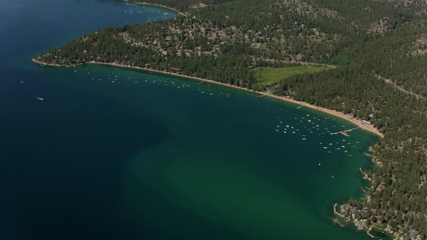 Boats sail in the water off the coast of a community surrounded by trees and forested mountains