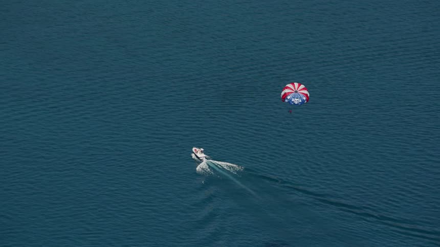 One of the several boats on water pulls parasail through air