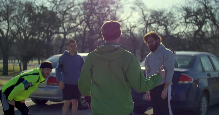 A group of men stretching and greeting each other in a parking lot on a cold day