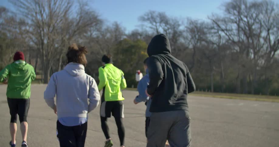 A group of men jog through a parking lot towards the trees