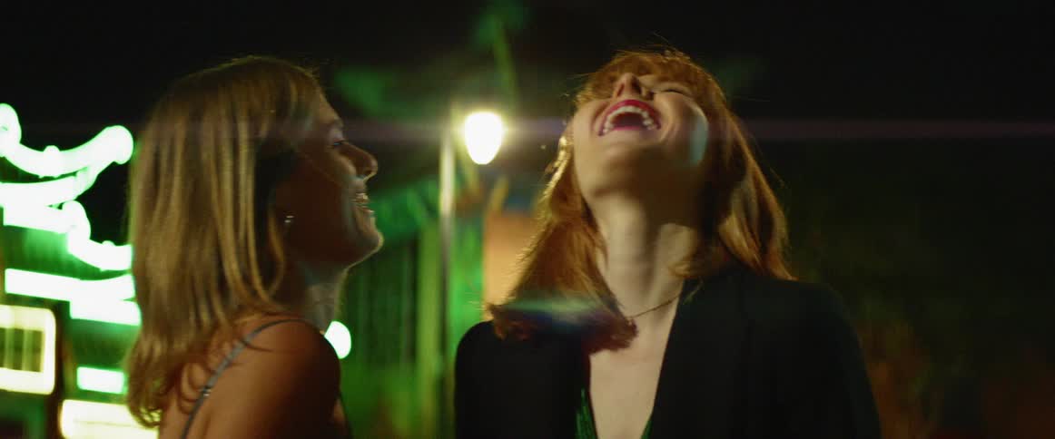 Two women smile and laugh on a city sidewalk