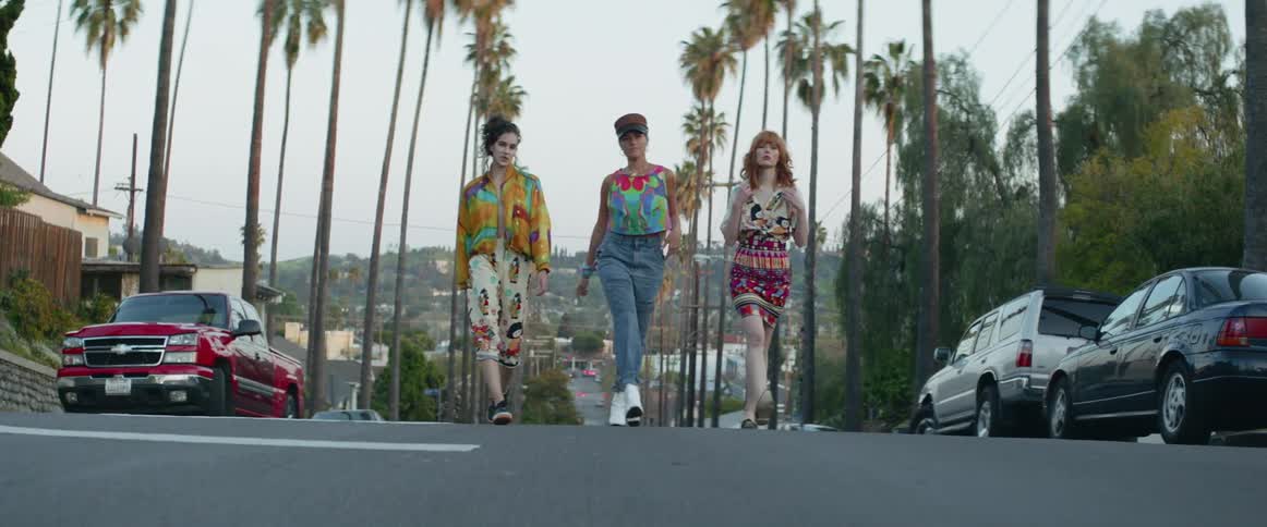 Young women walk down the middle of a street that is lined with palm trees