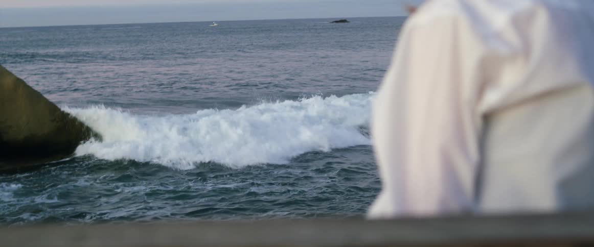 A woman sitting on the shore hugs her phone in to her chest