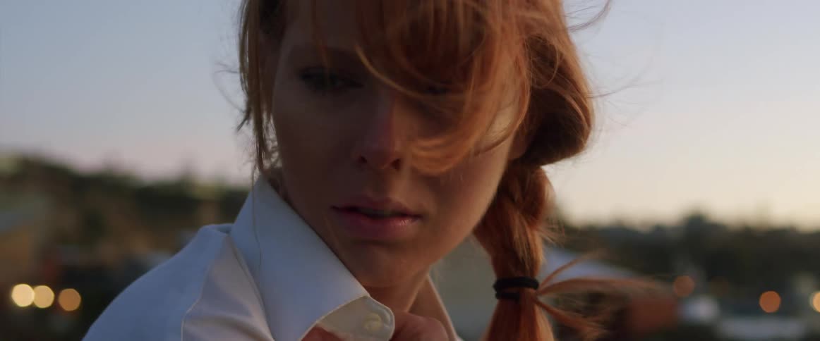 Woman smells the collar of her shirt while standing outdoors at sunset