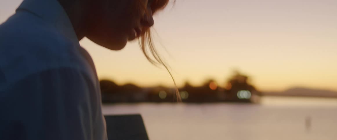 A young woman sitting on the shore writes in a notebook at dusk