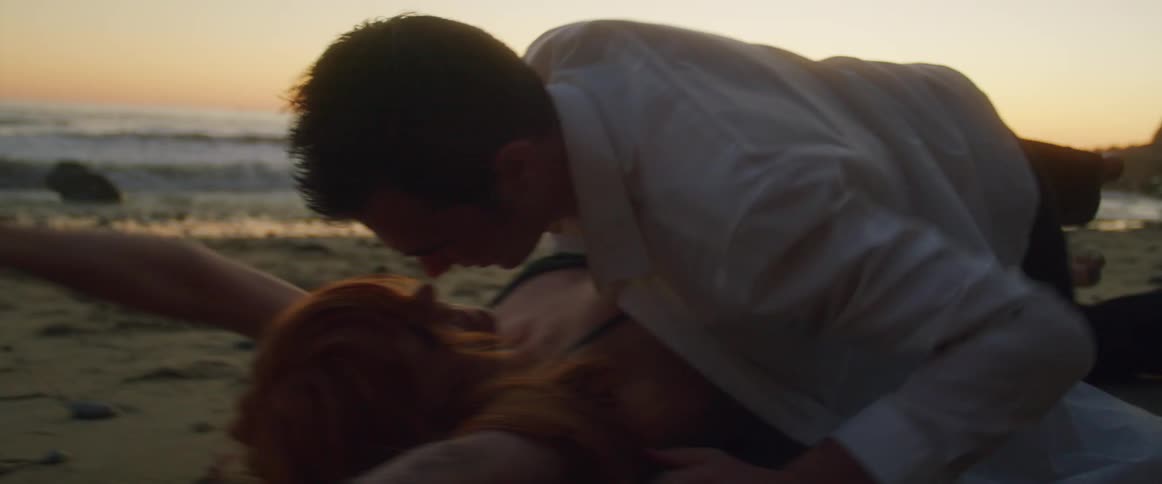 Young couple in formal clothes roll over the sand of a beach kissing each other at sunset