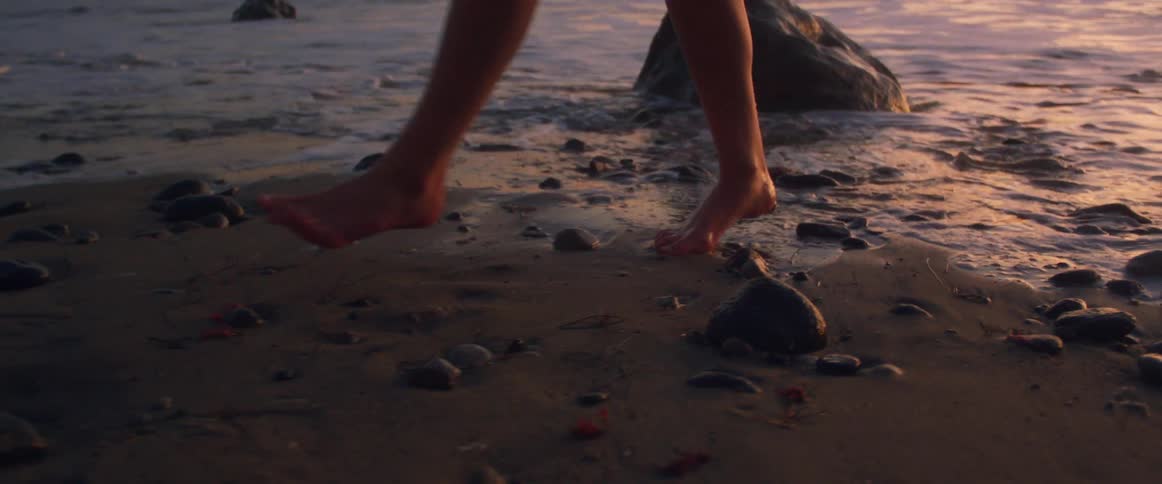 A white woman walks along a rocky beach