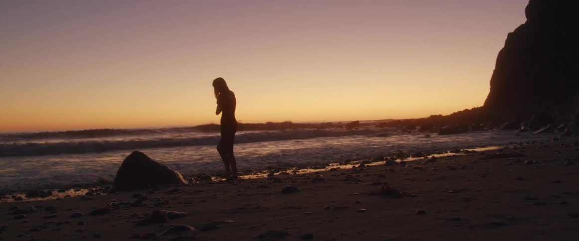 Woman walking around slowly in a relaxed way on the beach next to the sea is silhouetted against the red sky