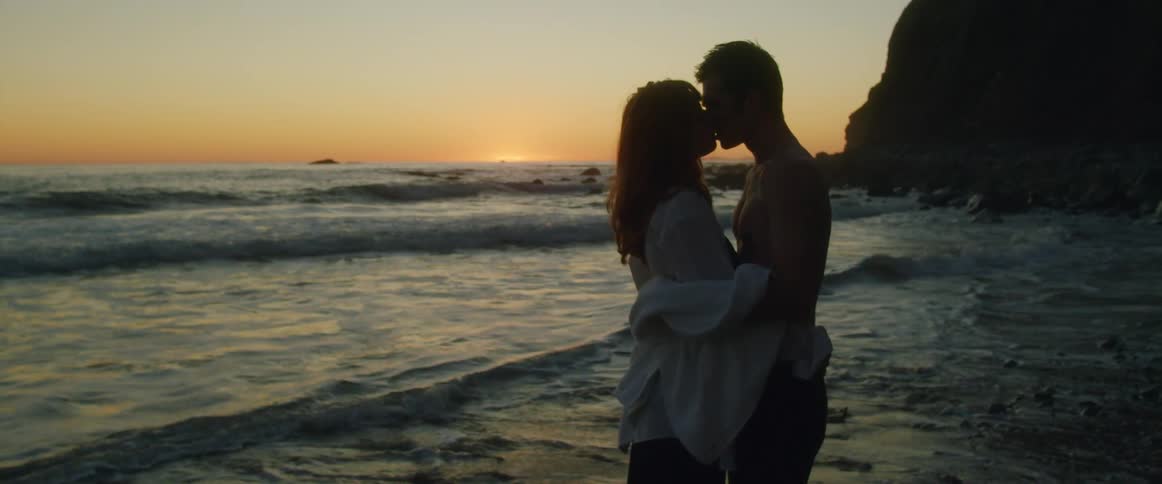 A man and woman kissing on the shore