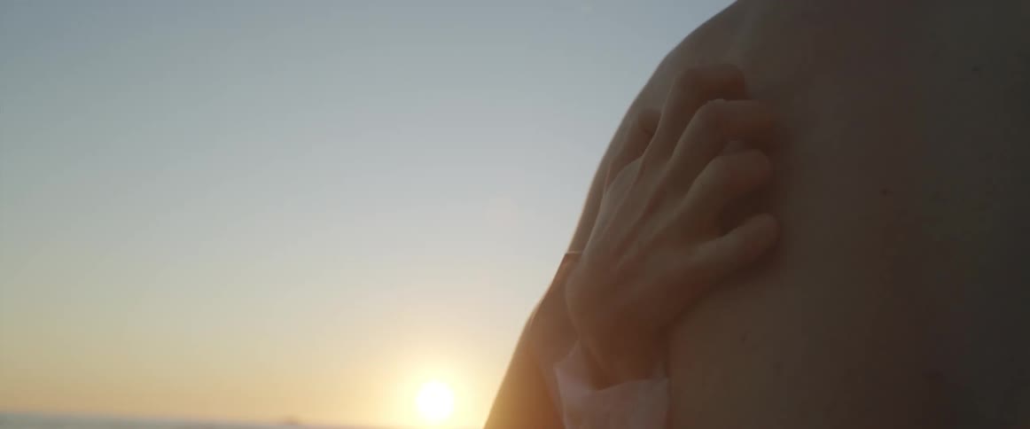 Woman grabs a mans back with her hand while hugging on the beach at sunset