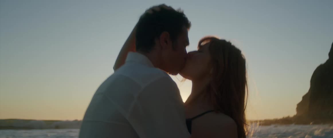 Young couple passionately kiss on the coastline of a beach at sunset