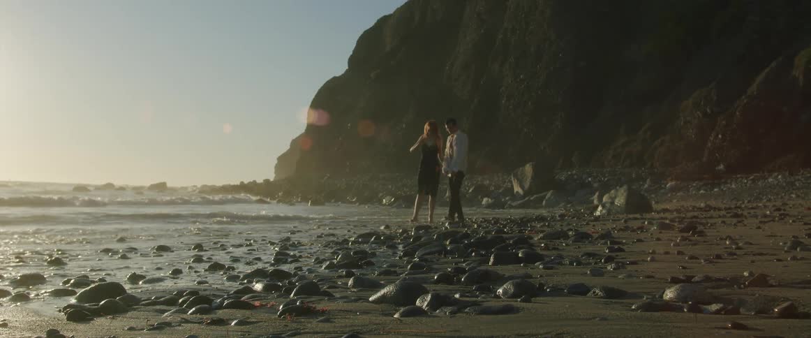 A man and woman are walking on the beach together at sunset