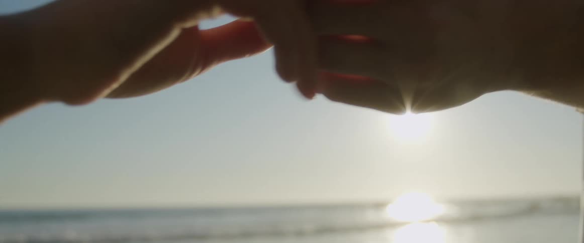 Couple lovingly hold hands in front of the ocean at sunset