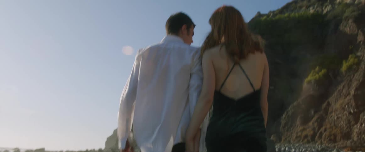 Man with a shirt pants and a woman with a black dress walk around slowly in a relaxed way on the beach