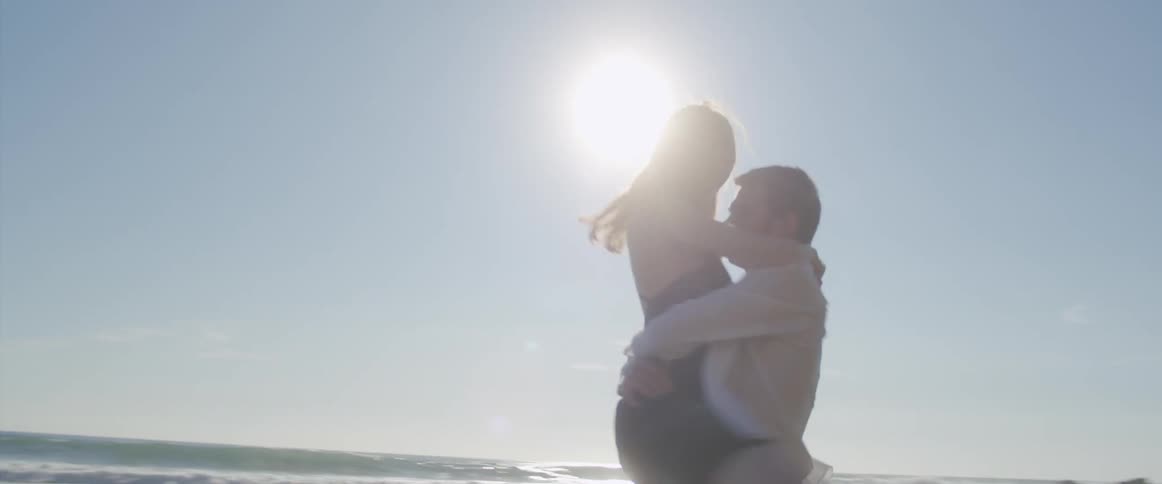 A woman jumps into the arms of a man standing on the beach and he spins around while carrying her in his arms