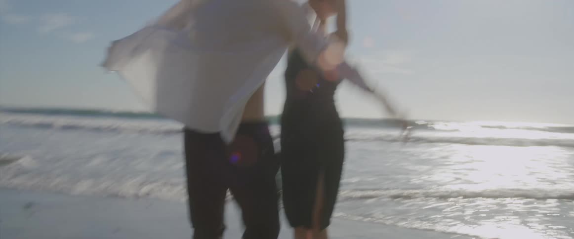 A man and woman dance together playfully on the beach