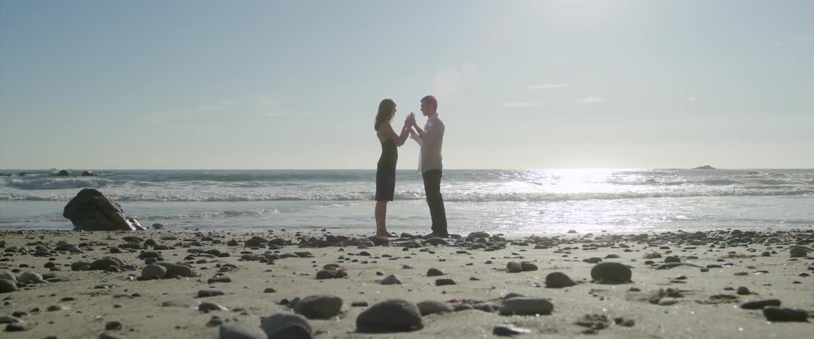 A man and woman stand and embrace on a beach