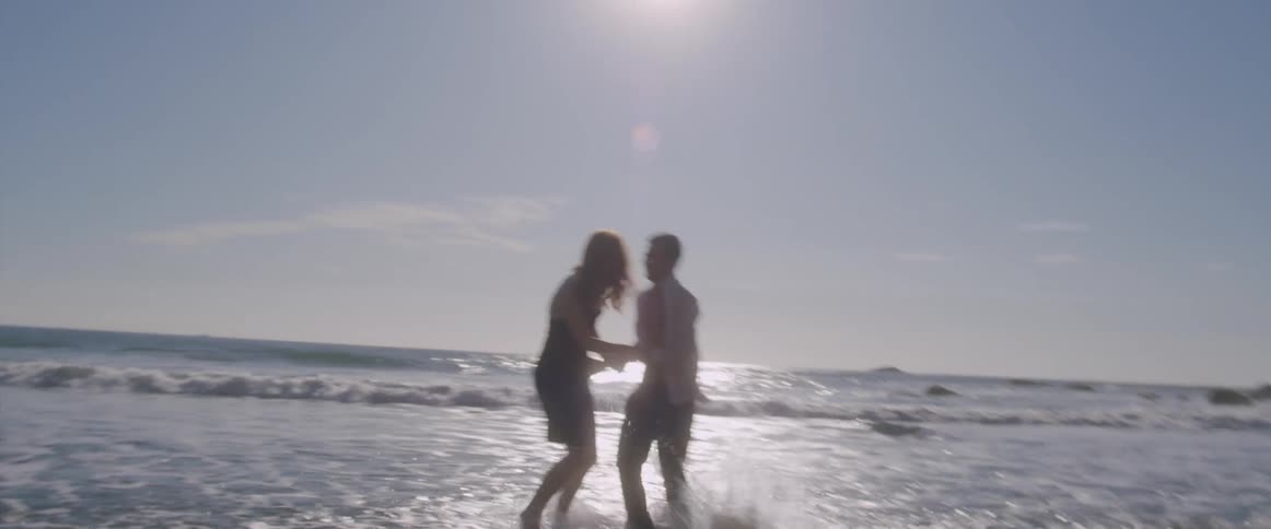 A man and woman run around and play together in the tide at the beach