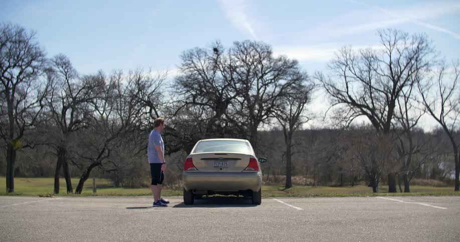 A man standing by a car outside on a sunny day