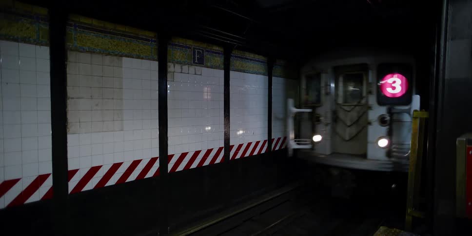 Lights glow and reflect on the subway tiles as the train comes through the tunnel
