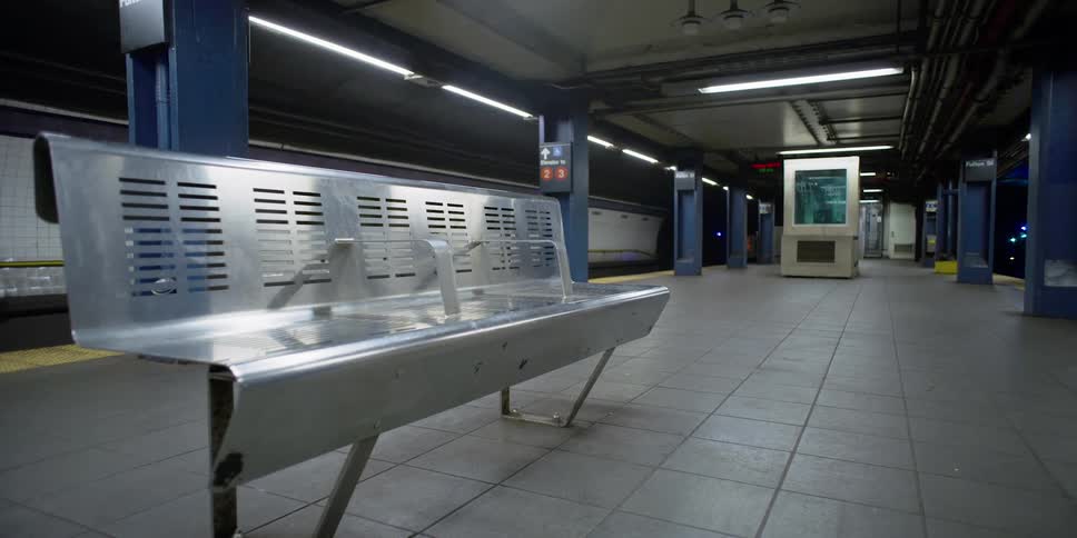 Fluorescent light glares off metal bench in transit station at night
