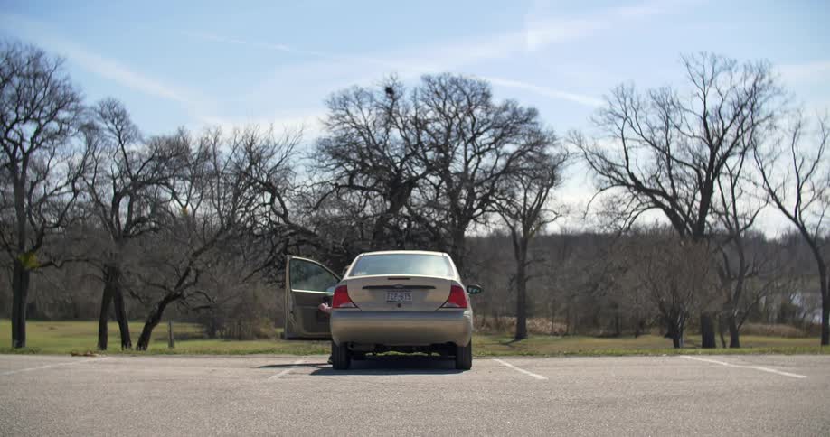 A man in a blue shirt and shorts opening a silver car door and getting in