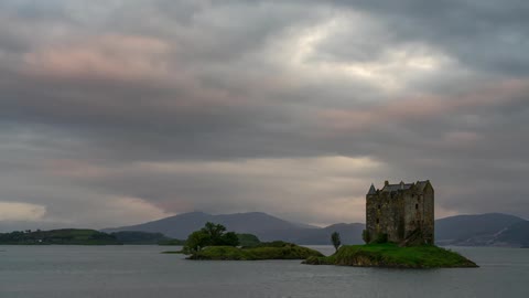 A castle on an island in the middle of a body water on a cloudy day
