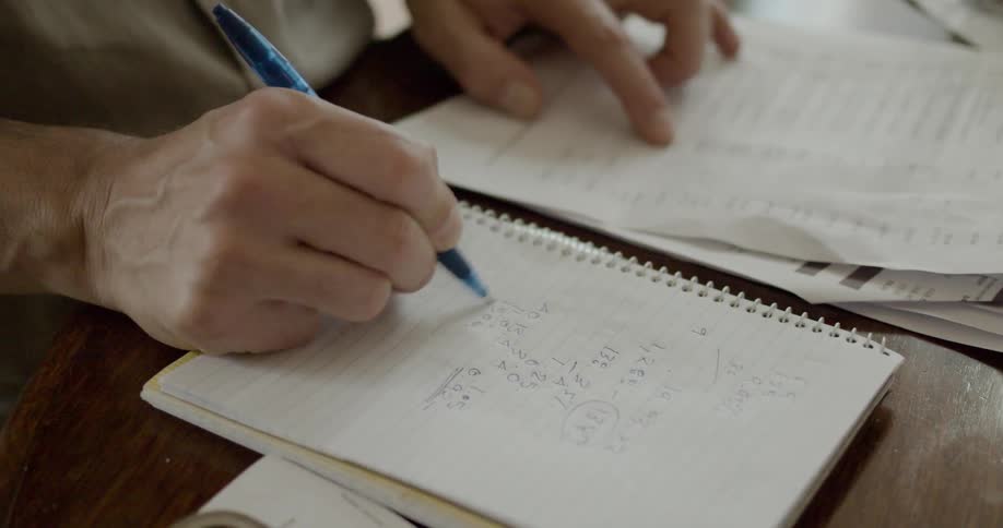 Someone reading notes from a paper and using a pen to do math on a notepad