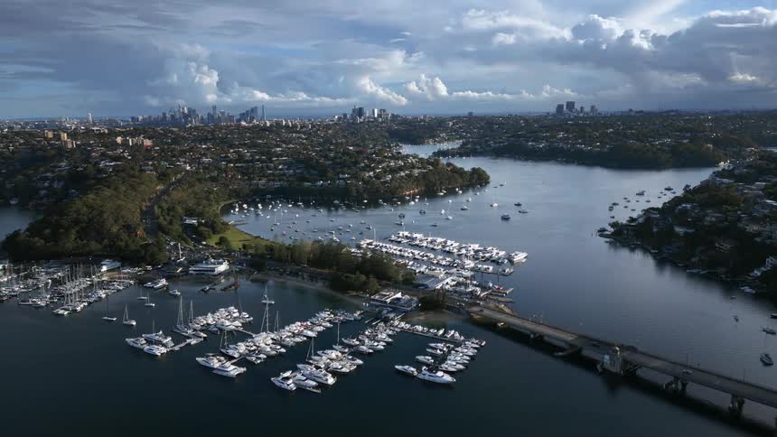 A marina full of boats at the end of a river connecting to land via a bridge