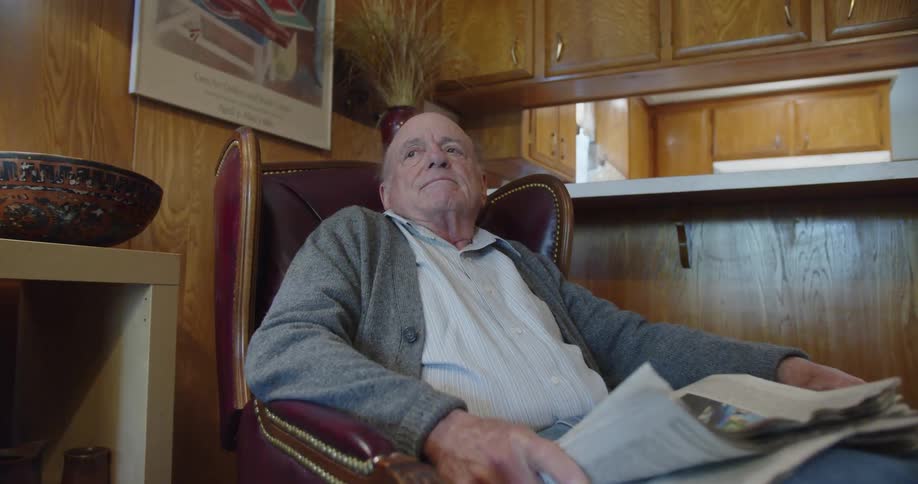 An old man reads a newspaper on a lounge chair puts the newspaper down takes off the glasses and closes his eyes in contemplation