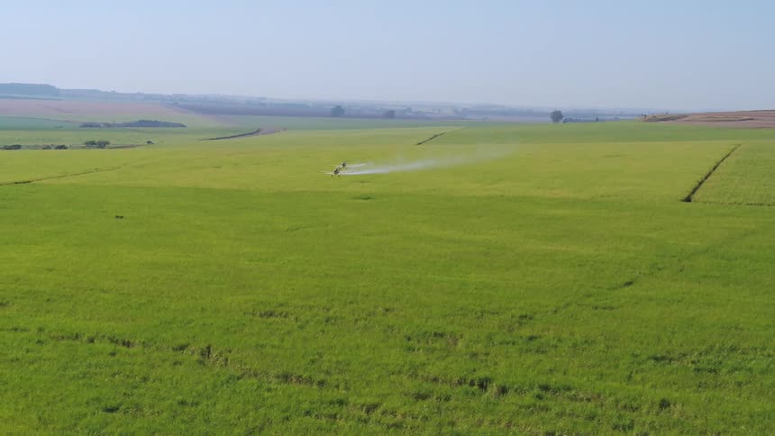Two small planes are flying over an open rural field with mountains in the distance