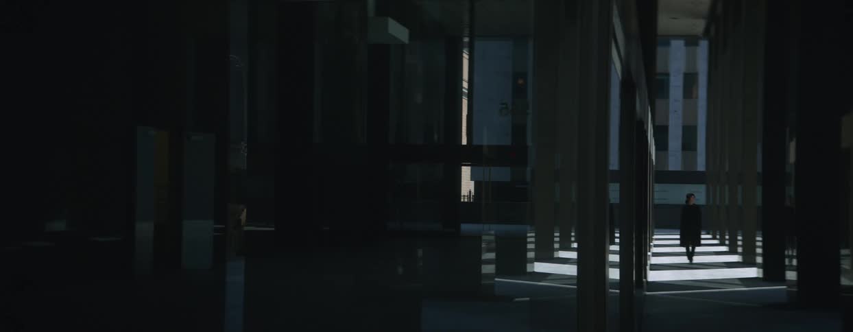 A woman in a sleek black ensemble stride among the towering pillars of a building