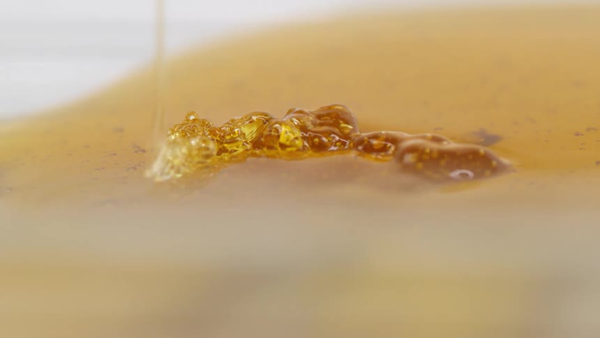 A line of honey drops down into a honey puddle on a white surface