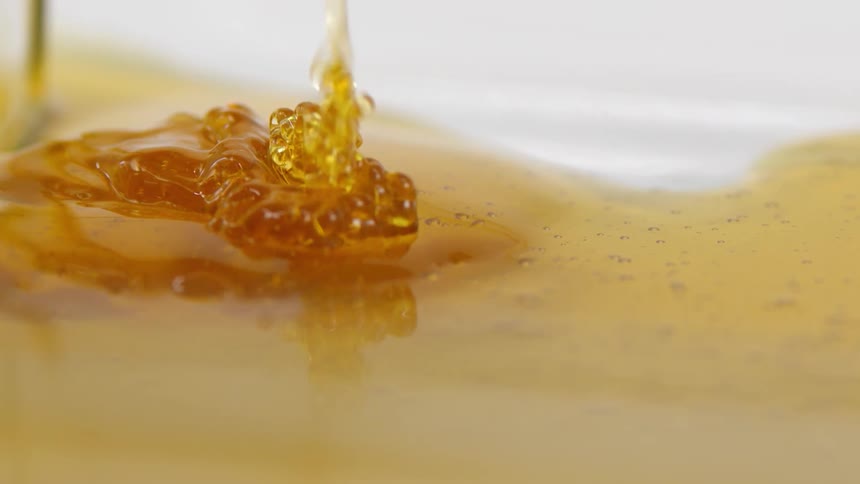 Golden honey is poured onto a smooth surface