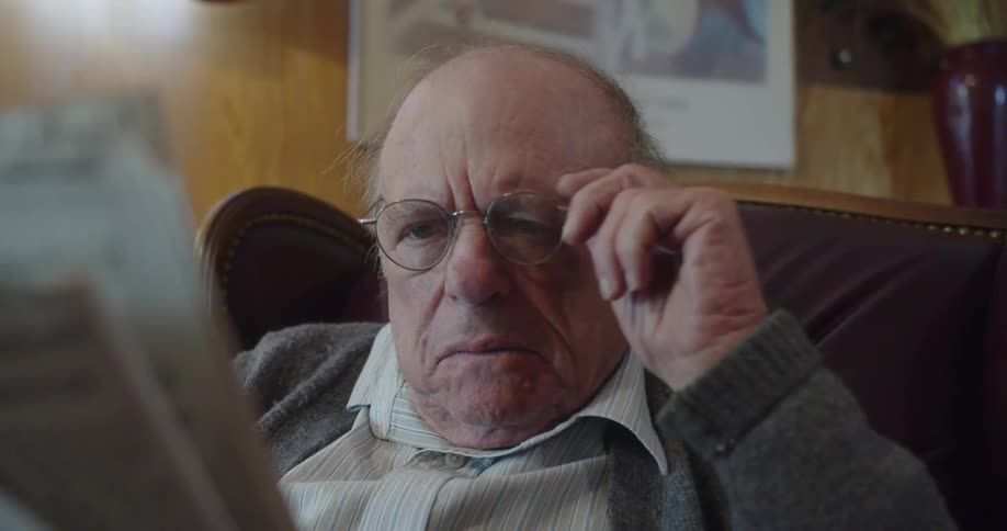 An elderly man is reading the newspaper in the day time