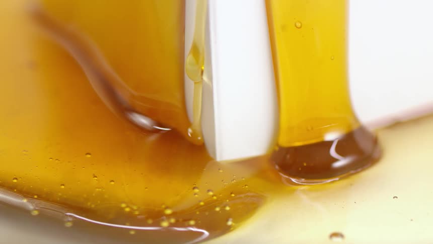 Honey oozing slowly down a white surface from two sides and connecting at the bottom