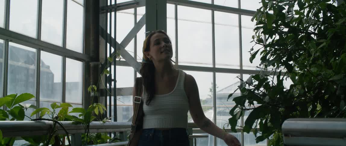 Young woman touches plants growing on a greenhouse in the city