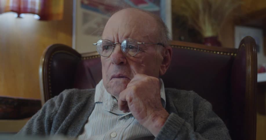 An old man is sitting on a lounge chair focused and intrigued while reading his newspaper