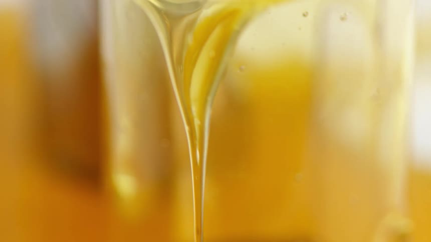 Light shines on a thick amber colored goopy liquid as it pours and drips