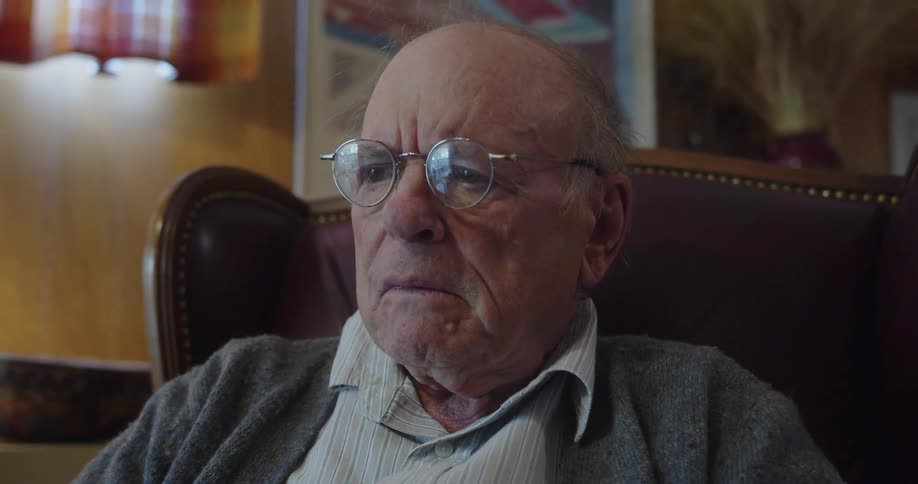 A man is sitting in a chair in his living room with a puzzled look on his face
