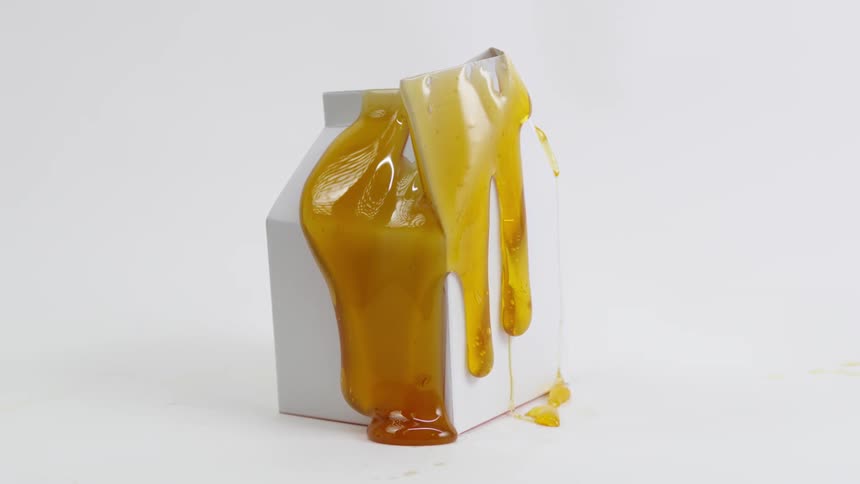 Honey dropped onto and then oozing down a milk carton