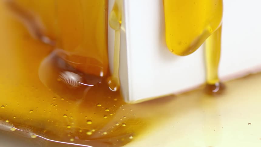 Amber syrup flows down sides of paper carton and onto hard surface