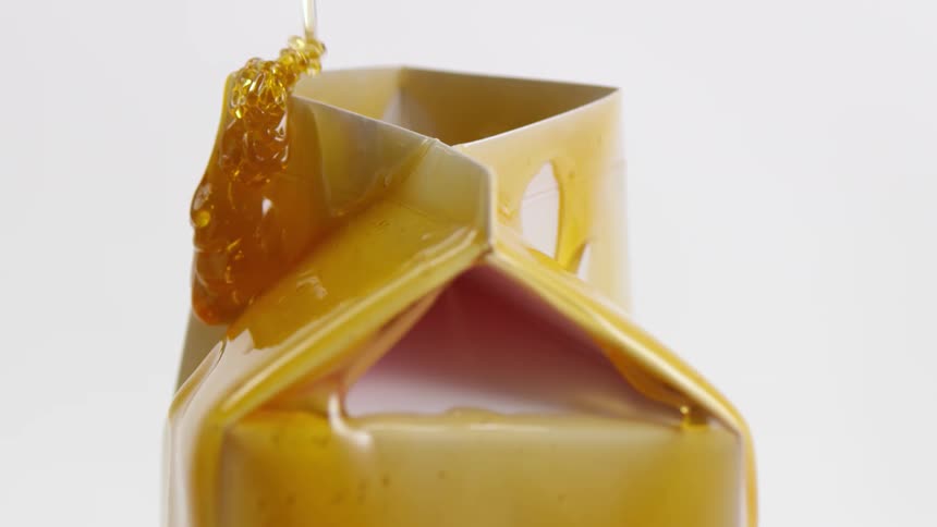 Honey being poured slowly over a white carton