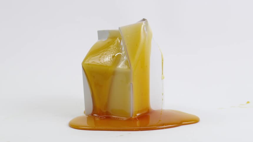 A goopy amber colored liquid flows and drips down the side of a carton into a puddle