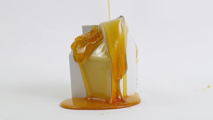 A white carton with honey being poured all over it as it drips down the sides