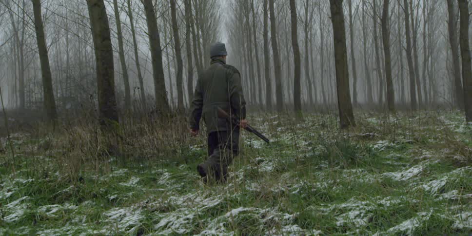 A man carries a hunting rifle through the woods