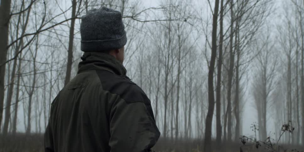 Man with a rifle standing in a forest on a winter day