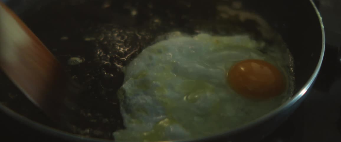 Person fries egg in skillet using a wooden spatula