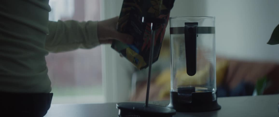 A woman is standing in the kitchen putting coffee grounds into a coffee pot