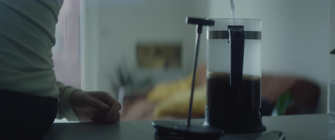 Woman in white shirt pours hot water in french press to make coffee